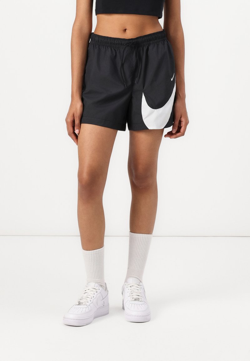 Melni sporta šorti ar elastīgu jostasvietu, ar lielu balto Nike swoosh un sānu šuvju kabatām. Apvienoti ar baltām kedām un zeķēm.