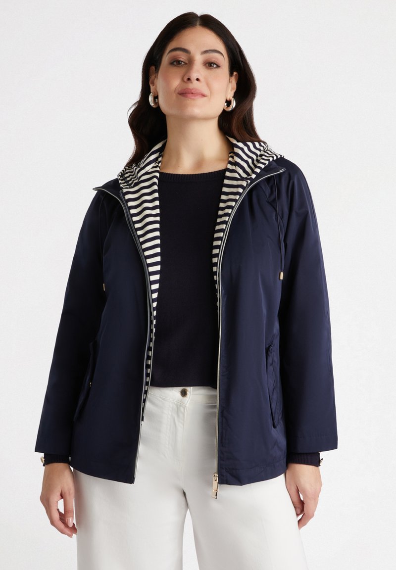 Veste légère bleu marine avec doublure de capuche rayée, fermeture éclair à l'avant, poches latérales et poignets côtelés. Texture lisse et design décontracté.