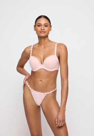Woman with medium skin tone wearing light pink floral lace-trimmed bra and matching high-cut panties, standing against a plain light background.