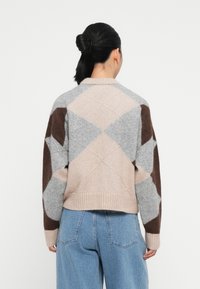 Maglione lavorato a maglia in grigio chiaro e beige con motivi a rombo marroni. Presenta un orlo e polsini a coste, con una silhouette rilassata.
