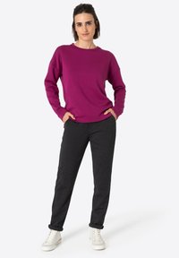 Fuchsia sweatshirt with a round neckline and dropped shoulders paired with dark gray tapered trousers and white lace-up sneakers.