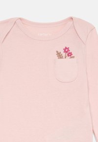 Light pink long-sleeve shirt, featuring a small pocket with pink flower and leaf embroidery. Soft fabric with a smooth texture.