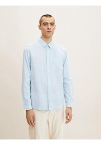 Camisa de manga larga azul claro con cuello abotonado, bolsillo frontal y una sutil textura. Fabricada con un tejido ligero.