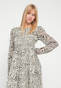 Langarmkleid in Creme mit schwarzem und braunem abstraktem Tierdruck, gerafftem Oberteil und fließendem Rock. Durchsichtige Ärmel und dezente Textur.