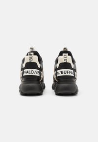 Schwarze und beige Sneakers mit einer robusten Sohle, die kontrastierende Streifen, Logo-Akzente, strukturierte Materialien und einen gepolsterten Kragen aufweisen.