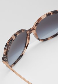 Ochelari de soare supradimensionați cu o montură din acetat în stil țestoasă și lentile gri cu degradé, având accente din metal aurit și un logo subtil pe braț.