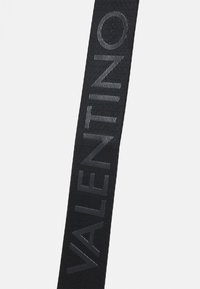 Svart tygrem med "VALENTINO"-logotypen i en strukturad, mörkgrå font, med en vävd struktur och en slank, förlängd form.