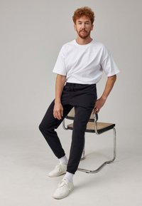 Witte katoenen T-shirt en zwarte joggers met een elastische tailleband. Witte sneakers met gestructureerde zolen. Eenvoudig ontwerp, casual pasvorm.