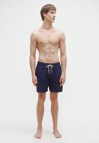 Herre badeshorts i marineblå med snor i midjen, laget av lett, hurtigtørkende stoff. Glatt tekstur med klassisk snitt, uten mønster.