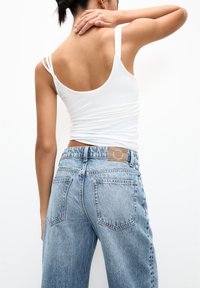 Weißes ärmelloses Top mit dünnen Trägern, kombiniert mit hochgeschnittenen, hellblauen Denim-Jeans mit verblasster Textur und zwei Gesäßtaschen.