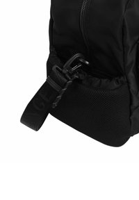 Zaino nero con un esterno in nylon liscio, una tasca laterale in rete e una tracolla testurizzata con lettering in rilievo.