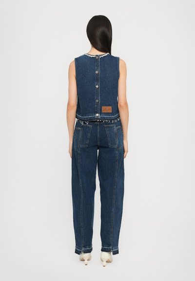 Salopetă din denim cu un top ajustat și pantaloni largi, cu un spate cu nasturi, cusături contrastante, margine disfăcută și o etichetă de marcă.