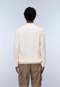 Licht crèmekleurige, lange mouw pullover met een geribbelde hals. Zacht materiaal, relaxte pasvorm, gecombineerd met beige cargobroek met zijzakken.