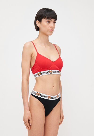 Soutien-gorge rouge à forme structurée, avec des fines bretelles et une bande logo Moschino. String noir avec une ceinture logo Moschino assortie.