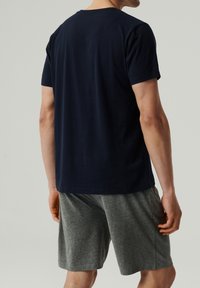 Granatowa koszulka z krótkim rękawem uszyta z miękkiej bawełny, zestawiona z szarymi szortami, o luźnym kroju i okrągłym dekolcie, widok od tyłu.