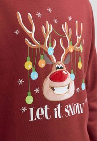 Bordeaux sweatshirt met een rendierafbeelding waarvan de hoorns versierd zijn met kleurrijke lichten, omringd door sneeuwvlokpatronen en de tekst "Laat het SNEEUWEN."