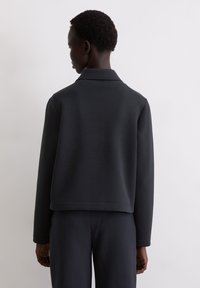  Czarna kurtka z polaru z kołnierzem, o luźnym kroju i ściągaczami na rękawach, widoczna od tyłu na neutralnym tle.