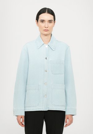 Light blue denim jacket featuring a pointed collar, front button closure, and two large patch pockets, with a relaxed fit and smooth texture.