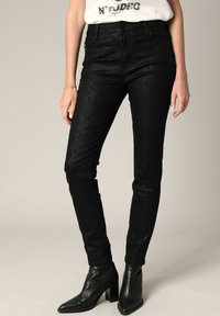 Jean noir ajusté avec un motif texturé en peau de serpent, taille haute et design à cinq poches, accompagné de bottines noires.