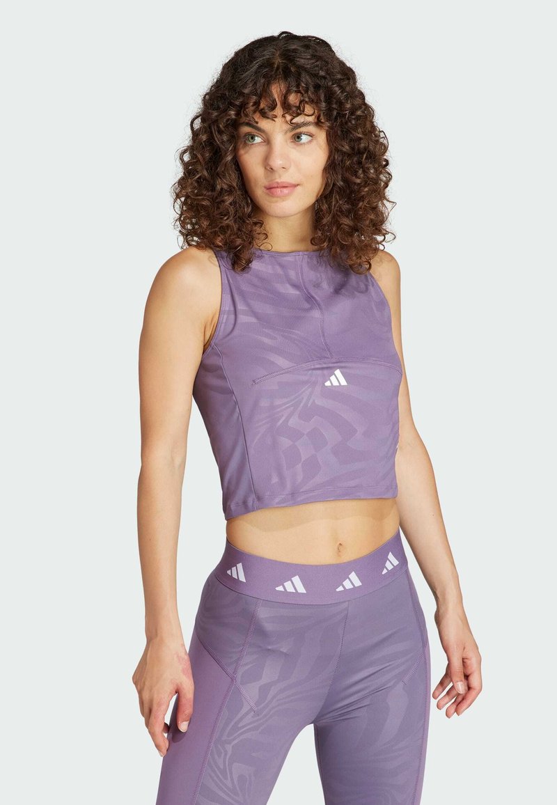 Lilla, cropped atletisk tanktop med en glat tekstur, der har et subtilt mønster og hvide logoaccentuer, parret med matchende leggings.