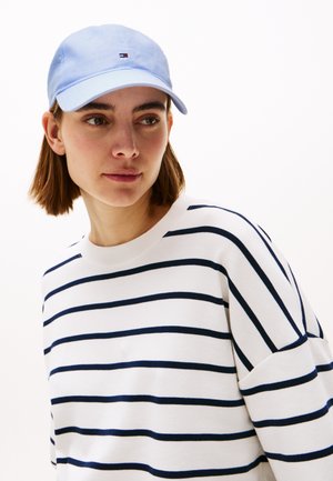 Light blue baseball cap with small logo, worn with a white shirt featuring navy horizontal stripes. Fabric appears soft with a relaxed fit.