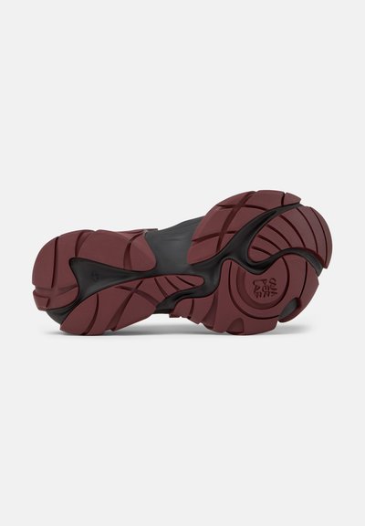 Sohle eines dunkelroten und schwarzen Sportschuhs mit tiefen Rillen, geschwungenen Profilmustern und strukturierter Haftung für verbesserte Traktion.