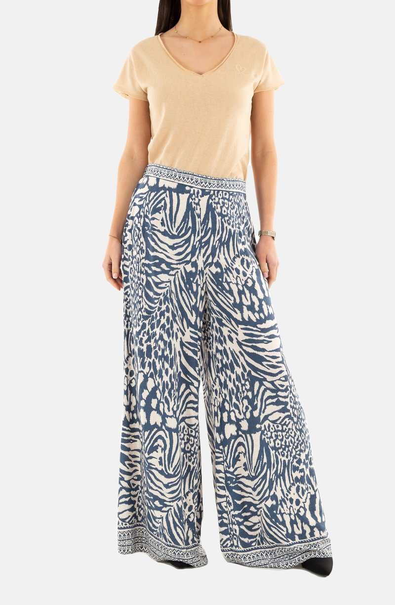 Pantaloni a gamba larga in blu e bianco, caratterizzati da una vivace stampa animale e una vita decorata. Abbinati a una t-shirt beige a scollo a V.