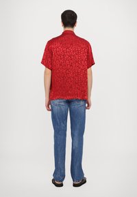 Rode kortemouwen shirt met leopardprint ontwerp, gemaakt van glanzende stof. Gecombineerd met vervaagde blauwe jeans en zwarte sandalen.