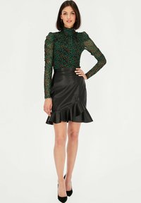 Bluzka w zielono-czarny panterkowy wzór z wysokim kołnierzem, w połączeniu z czarną spódnicą z sztucznej skóry z falbaną na dolnej krawędzi.