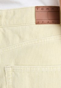 Svijetložute kordne hlače s vertikalnim rebrima, detaljem na džepu i smeškim kožnim etiketom s urezanim natpisom "TOMMY JEANS."