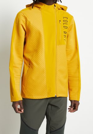 Mann trägt einen leuchtend gelben Zip-Hoodie mit dem Schriftzug „COLD.RDY“ auf der Brusttasche und dunkelgraue Hose.