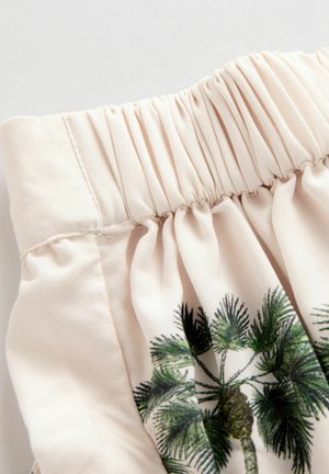 Tissu beige clair avec taille élastique froncée et motif de palmier vert. Texture lisse avec des détails de couture subtils.
