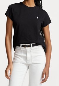 T-shirt en coton noir à manches courtes et décolleté rond, avec un petit logo blanc sur la poitrine gauche ; associé à un pantalon en denim blanc.