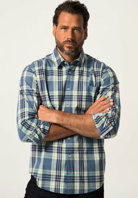 Camicia a scacchi blu e verde con bottoni, maniche lunghe arrotolate e taschino sul petto. Realizzata in un tessuto liscio con un motivo a quadri.
