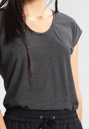 Maglietta a maniche corte a righe bianche e nere con scollatura rotonda, realizzata in tessuto morbido, indossata sopra pantaloni neri con vita elastica.