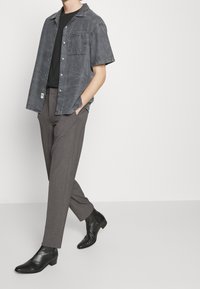 Grijs T-shirt met korte mouwen en een zakje, gecombineerd met donkergrijze geplooide broek en zwarte leren laarzen met een spitse neus en gestikte details.