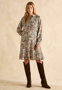 Blumenmusterkleid mit langen Ärmeln, einem Kragen und gerafftem Rock. Kombiniert mit braunen Wildleder-Stiefeln bis zum Knie. Strukturierten Stoff.