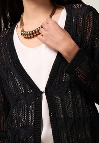 Cardigan nero lavorato a maglia con un design a trama aperta e decorata, dotato di un profondo scollo a V e di una chiusura con un singolo bottone sul davanti.
