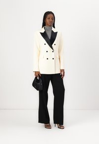 Divraku uzvalks krēmkrāsā ar melnā krāsa apmali, apvienots ar pelēku turtleneck, melniem platām biksēm un melnu rokassomu. Modelis valkā augstpapēžu sandales.
