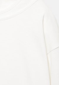 Weißer Pullover aus glattem, weichem Material mit weiter Halslinie und überschnittenen Schultern, die eine lässige Passform und ein klares Design betonen.