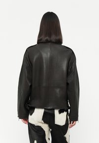 Black leather jacket with a relaxed fit, visible seams, and zippered cuffs, paired with cow-print textured pants.