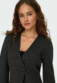 Sivi kardigan izrađen od mekog pletenog materijala. Ima duboki V-izrez i zatvaranje na jedan dugmić. Elegantan dizajn s udobnim krojem.