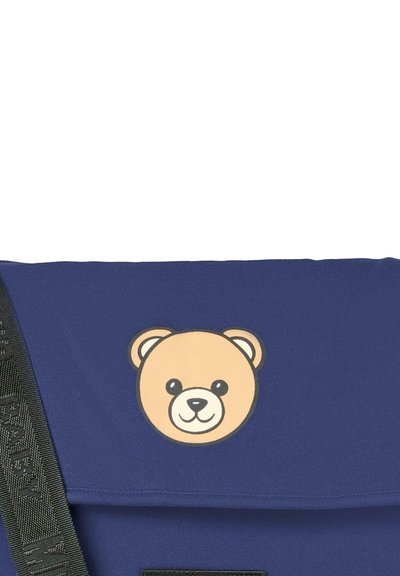 Borsa a tracolla blu con grafica di un volto d'orso sulla patta. Presenta una tracolla texturizzata con accessori neri e una finitura in tessuto liscio.