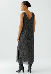 Robe maxi noire avec un décolleté en V et un motif tourbillonnant blanc détaillé. Elle possède des fentes latérales et est accompagnée de bottes noires montantes.