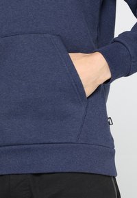 Felpa blu navy con tasca a marsupio e polsini a coste. Realizzata in tessuto morbido con una piacevole texture liscia. Include un piccolo dettaglio con etichetta.