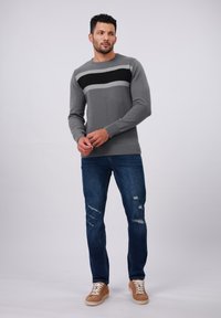 Gray sweater with a black and light gray horizontal stripe, paired with distressed blue jeans and tan sneakers, all on a plain background.