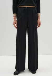 Black wide-leg trousers made of smooth fabric, featuring a front button closure, two side pleats, and a tailored fit.