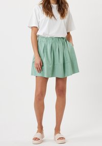 Fållad mintgrön kjol med elastisk midja, tillverkad av mjukt tyg, ihopparad med en vit t-shirt och ljusfärgade plattformssandaler.