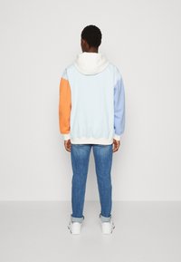 Felpa con pannelli color block in blu chiaro, arancione e blu pastello, in tessuto di cotone, veste comoda e con cappuccio bianco con cordino. Abbinata a jeans.