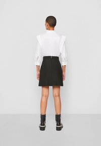 Valkoinen paita olkatoppauksilla, pitkät hihat ja leikkaukset, yhdistetty mustaan liehuvaan hameeseen, päällä mustat nilkkurit.